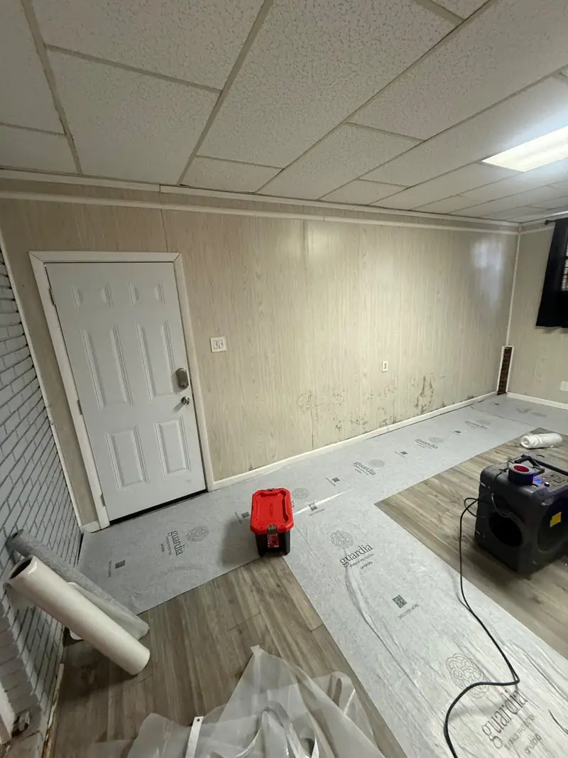 Basement mid-rebuild: new wall going up, floor covered, air scrubber running