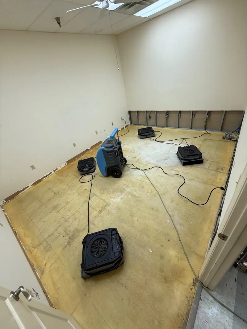 Bare subfloor room with drywall cut low, air movers and a dehumidifier running