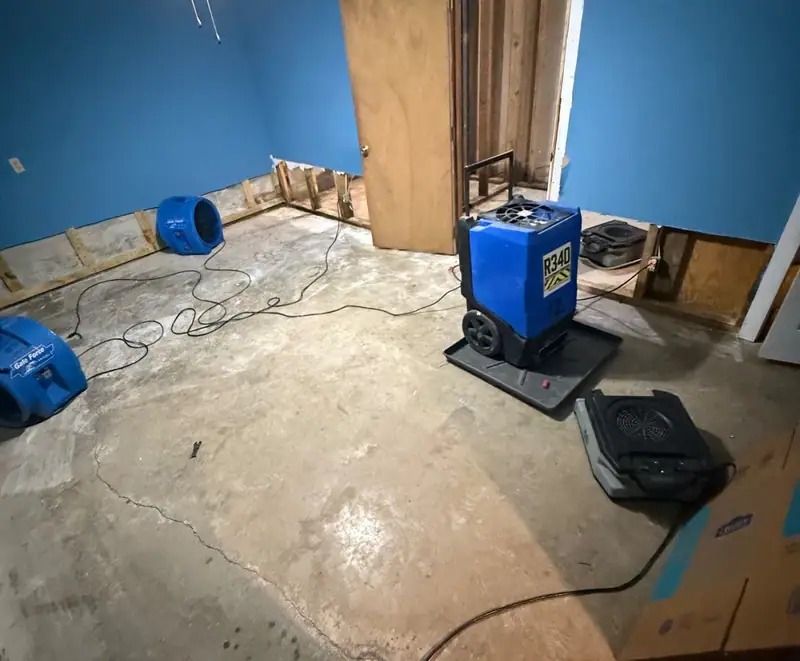 Dehumidifier and air movers in a blue bedroom with the bottom of the drywall cut away