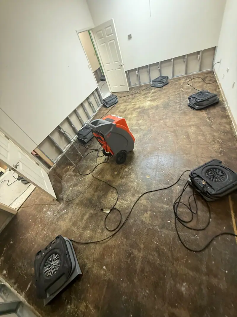 Air movers and a dehumidifier drying a subfloor, drywall cut out along the walls