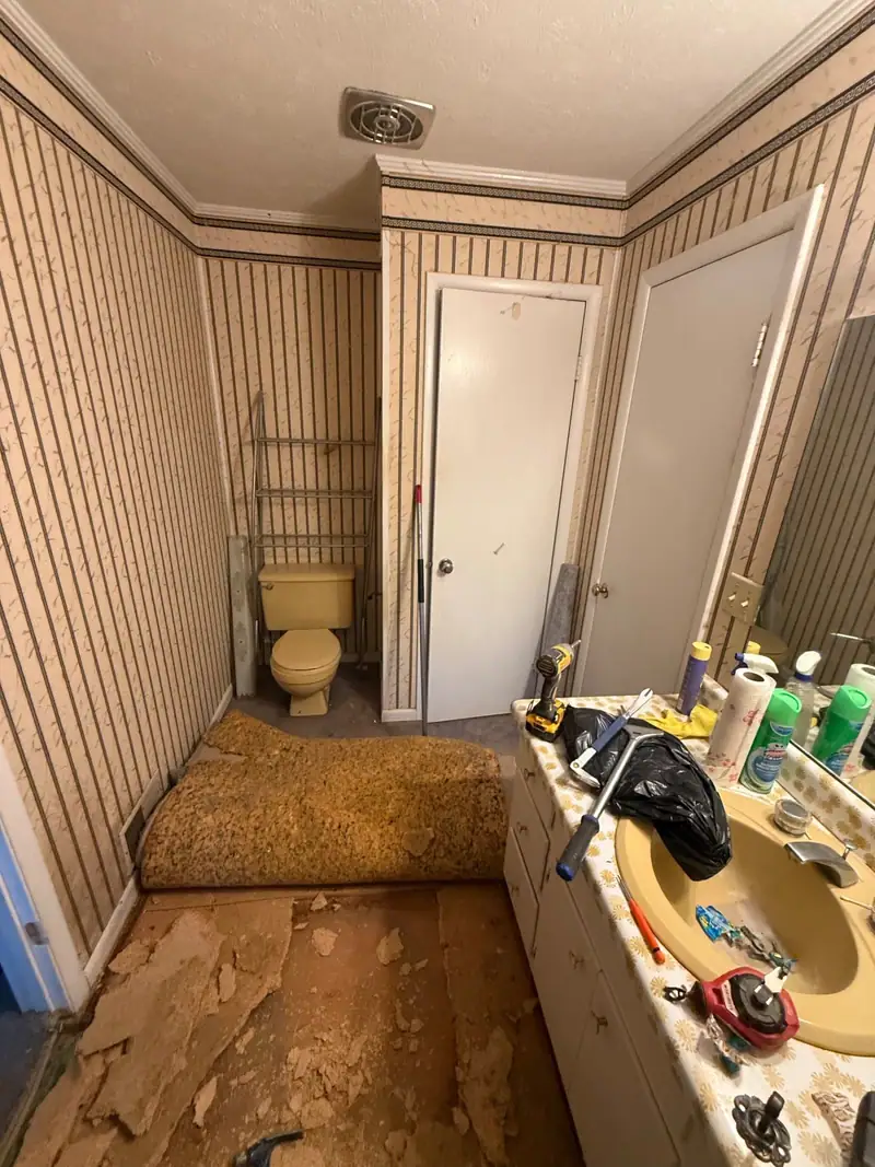 Bathroom floor torn out to the subfloor with the carpet rolled back